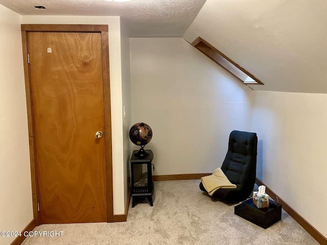 sitting room with a textured ceiling, lofted ceiling with skylight, baseboards, and light colored carpet