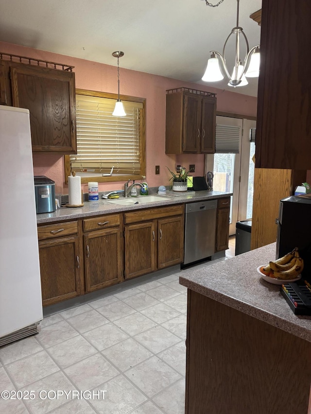 kitchen featuring dishwasher, freestanding refrigerator, a sink, pendant lighting, and a chandelier