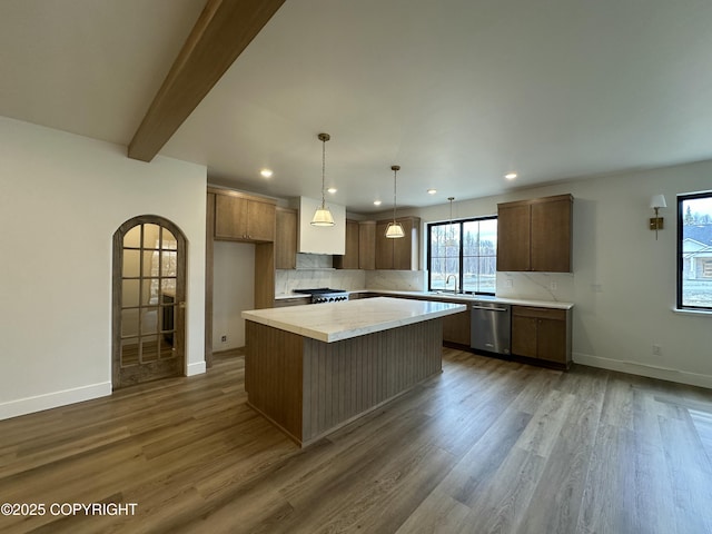 kitchen with stainless steel dishwasher, a center island, light countertops, backsplash, and dark wood-style flooring