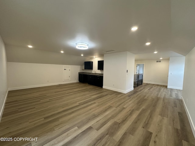 unfurnished living room with recessed lighting, wood finished floors, visible vents, a sink, and baseboards