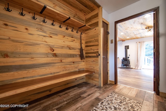 mudroom with wooden walls, a sauna, wood ceiling, wood finished floors, and a wood stove