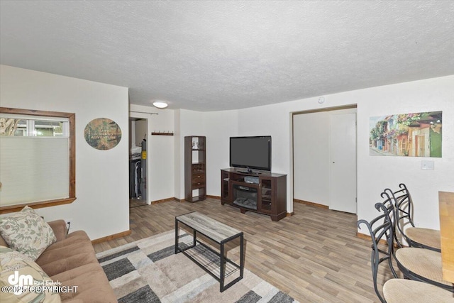 living room featuring a textured ceiling, light wood-type flooring, and baseboards