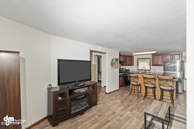 living area featuring a textured ceiling, baseboards, and light wood-style floors