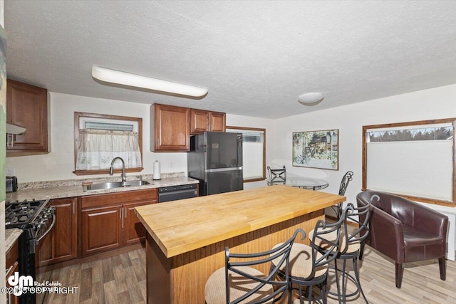 kitchen featuring a breakfast bar, a sink, wood counters, wood finished floors, and black appliances