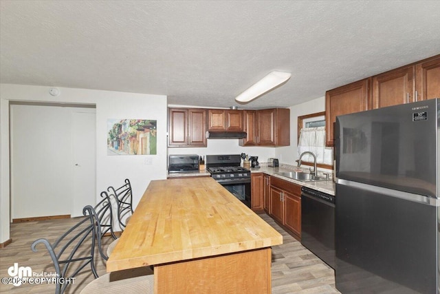 kitchen featuring light wood-style flooring, under cabinet range hood, a sink, wooden counters, and black appliances