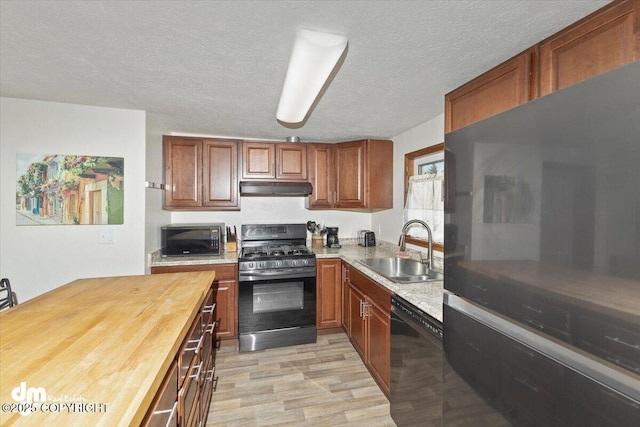 kitchen featuring light wood-style flooring, wood counters, under cabinet range hood, black appliances, and a sink