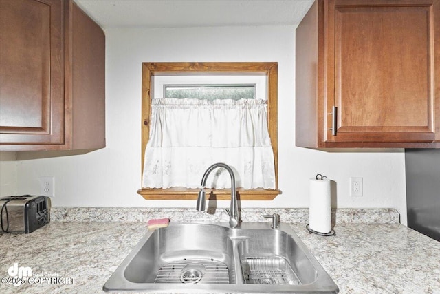 kitchen featuring brown cabinetry, a toaster, a sink, and light stone counters