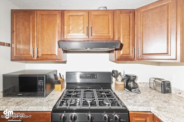 kitchen with light countertops, brown cabinets, range with gas cooktop, and under cabinet range hood