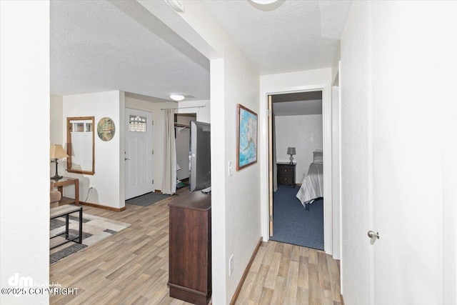 hallway with light wood-type flooring, baseboards, and a textured ceiling