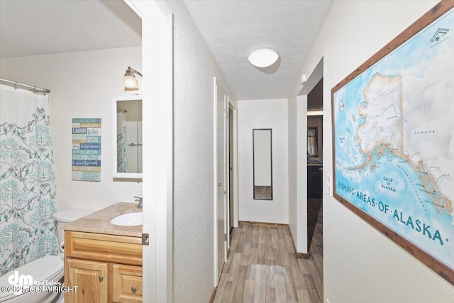 hall featuring a textured ceiling, a sink, and light wood-style floors