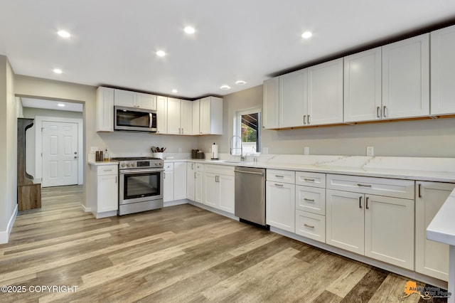 kitchen with recessed lighting, light wood-style flooring, appliances with stainless steel finishes, white cabinetry, and a sink