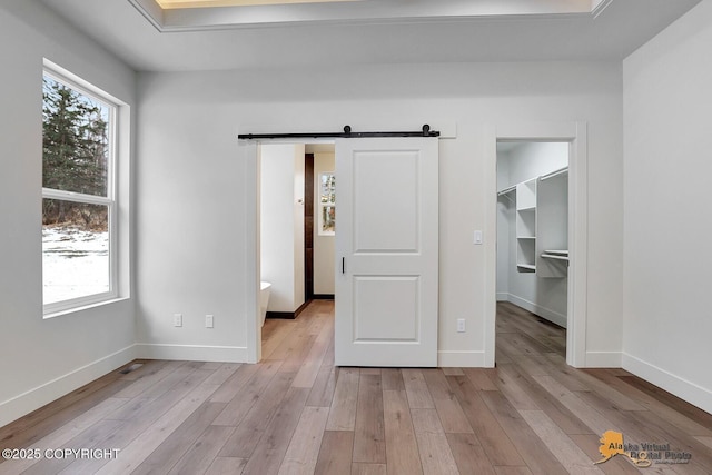 unfurnished bedroom with a barn door, multiple windows, light wood-type flooring, and a walk in closet