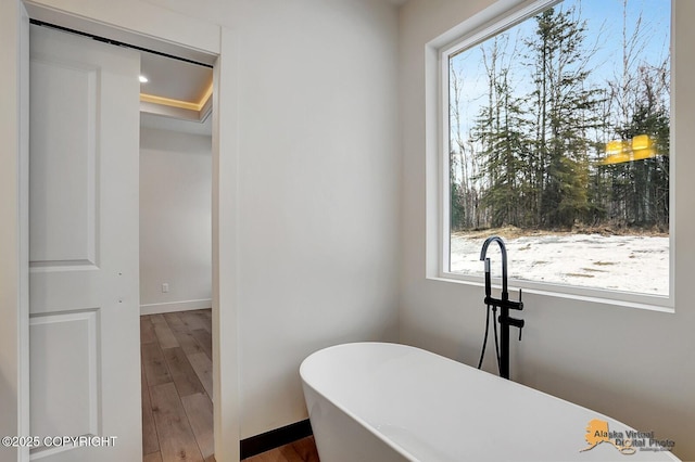 full bathroom featuring a soaking tub, baseboards, and wood finished floors