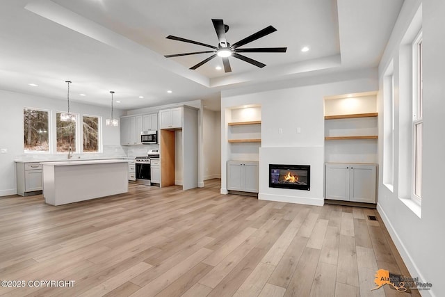 unfurnished living room with light wood-type flooring, a tray ceiling, a glass covered fireplace, and recessed lighting