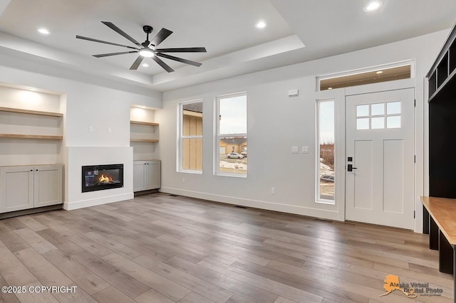 foyer with baseboards, a glass covered fireplace, wood finished floors, a tray ceiling, and recessed lighting