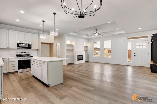 kitchen with light wood-type flooring, appliances with stainless steel finishes, light countertops, and a tray ceiling