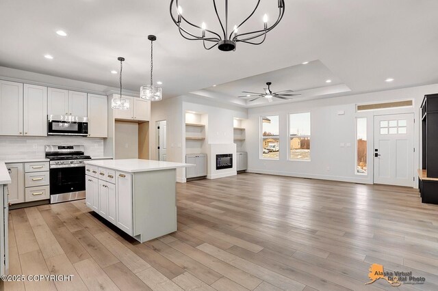 kitchen with light wood finished floors, light countertops, appliances with stainless steel finishes, and a raised ceiling