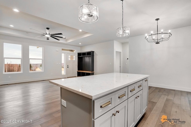 kitchen featuring baseboards, open floor plan, a center island, a tray ceiling, and light wood-type flooring