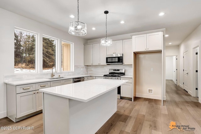 kitchen featuring tasteful backsplash, a kitchen island, appliances with stainless steel finishes, light wood-type flooring, and a sink