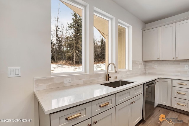 kitchen with tasteful backsplash, dishwasher, light stone counters, wood finished floors, and a sink