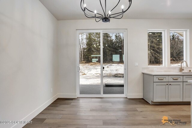 doorway to outside with light wood-style floors, a notable chandelier, a sink, and baseboards