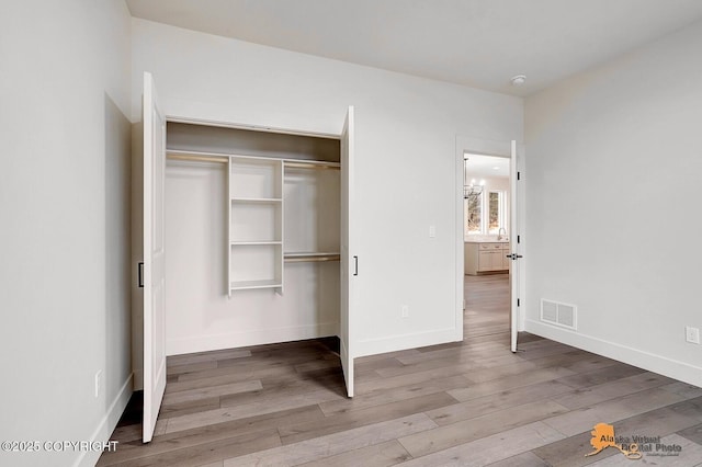 unfurnished bedroom with a closet, visible vents, baseboards, and wood finished floors