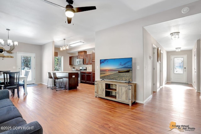 living room featuring ceiling fan with notable chandelier, light wood-style flooring, and baseboards