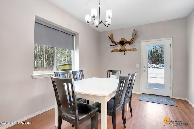 dining area with light wood-type flooring, baseboards, and an inviting chandelier