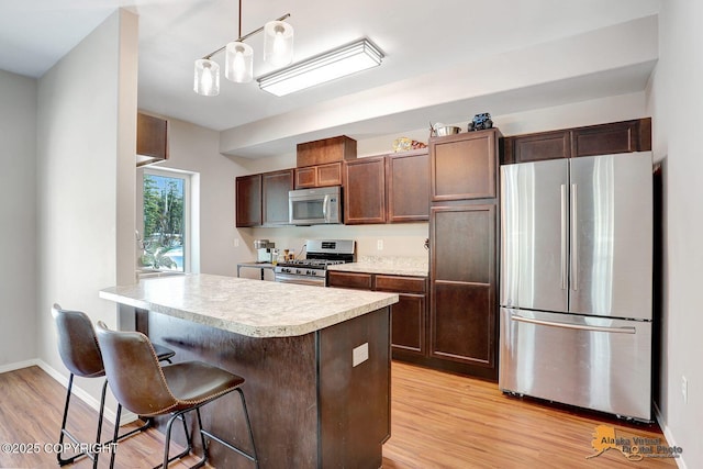 kitchen featuring baseboards, light countertops, appliances with stainless steel finishes, light wood finished floors, and a kitchen bar