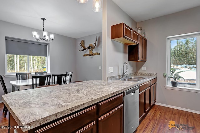 kitchen with a peninsula, wood finished floors, a sink, light countertops, and dishwasher