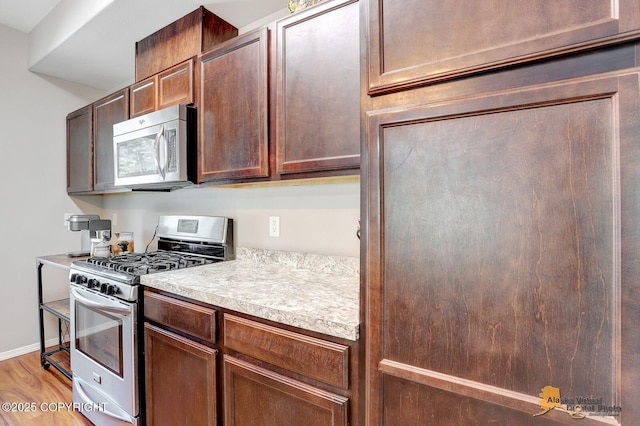 kitchen featuring appliances with stainless steel finishes, light countertops, light wood-style flooring, and baseboards