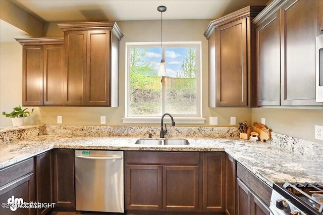 kitchen featuring appliances with stainless steel finishes, a sink, light stone countertops, and hanging light fixtures
