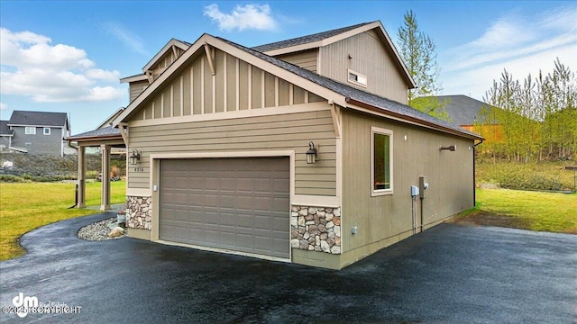 view of property exterior with stone siding, a garage, a yard, and asphalt driveway