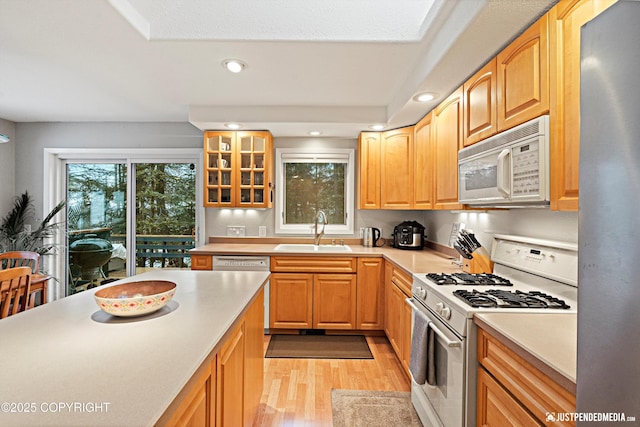 kitchen with white appliances, glass insert cabinets, light countertops, light wood-style floors, and a sink