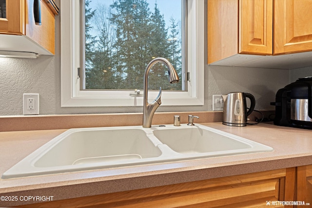 kitchen featuring a textured wall, light countertops, and a sink