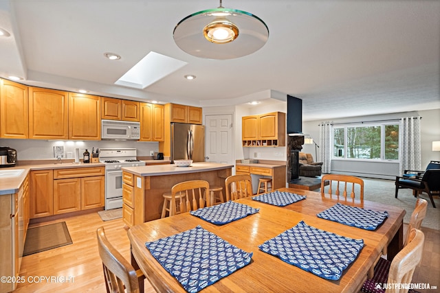 dining room featuring a skylight, a baseboard radiator, light wood-style flooring, and recessed lighting