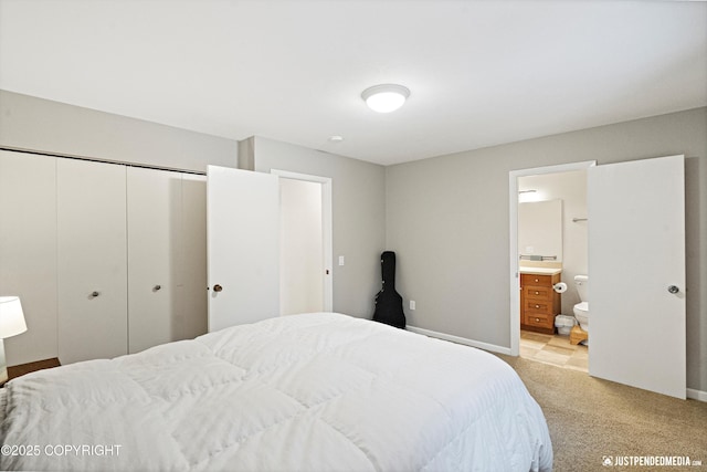 bedroom with a closet, light colored carpet, baseboards, and ensuite bathroom