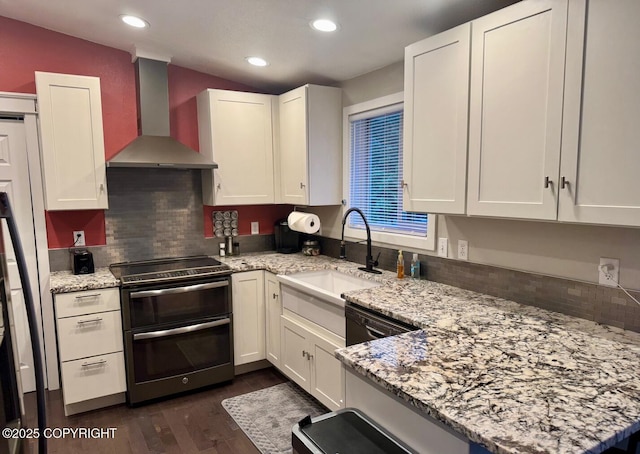 kitchen with white cabinets, wall chimney exhaust hood, light stone countertops, double oven range, and a sink