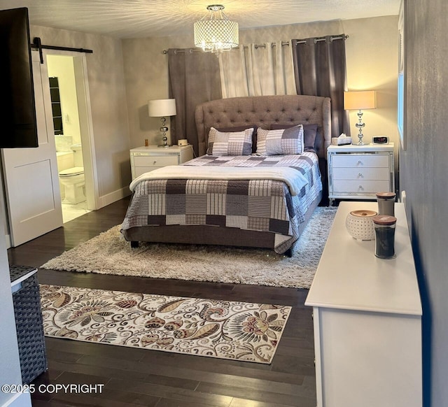 bedroom featuring a chandelier, wood finished floors, connected bathroom, and a barn door