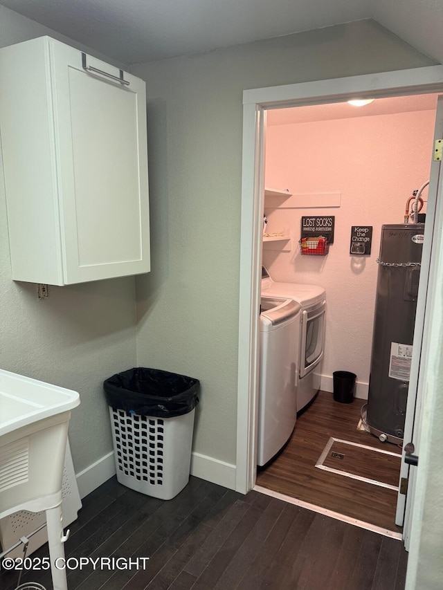 clothes washing area featuring dark wood-style flooring, baseboards, water heater, cabinet space, and washing machine and clothes dryer