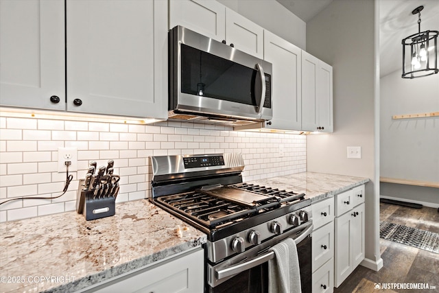 kitchen with appliances with stainless steel finishes, dark wood-type flooring, light stone counters, and decorative backsplash