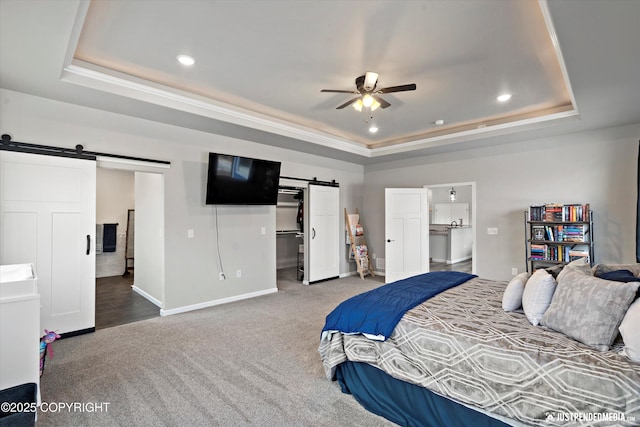 bedroom with a barn door, baseboards, a spacious closet, a tray ceiling, and carpet flooring