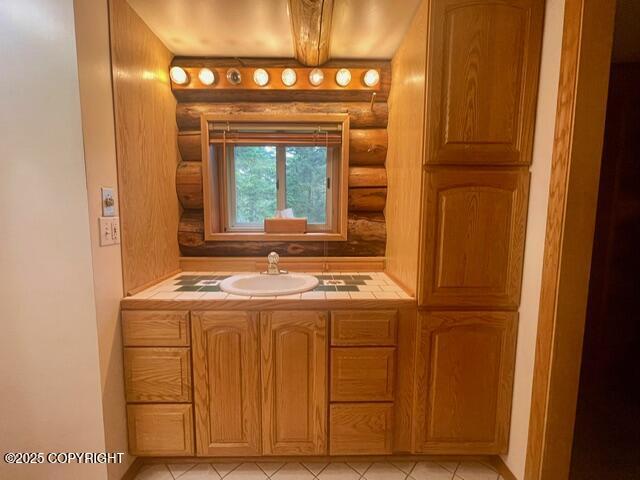 bathroom with beam ceiling, rustic walls, tile patterned flooring, and vanity