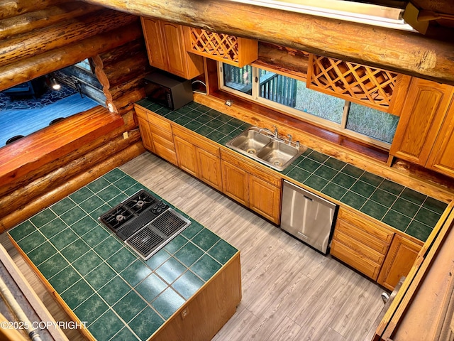 kitchen with rustic walls, stainless steel dishwasher, tile counters, and a sink