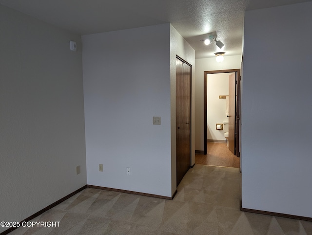 hall featuring light colored carpet, baseboards, and a textured ceiling