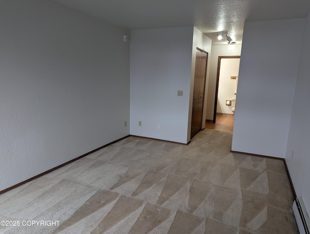 spare room with a baseboard heating unit, baseboards, and light carpet