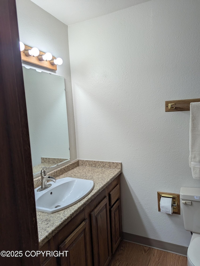 bathroom featuring baseboards, toilet, wood finished floors, and vanity