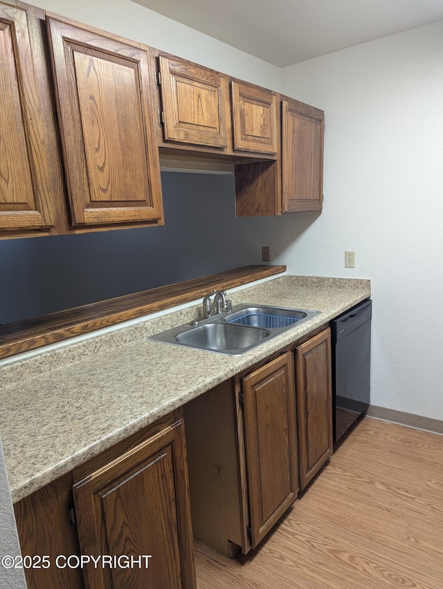 kitchen featuring light wood finished floors, a sink, black dishwasher, light countertops, and baseboards