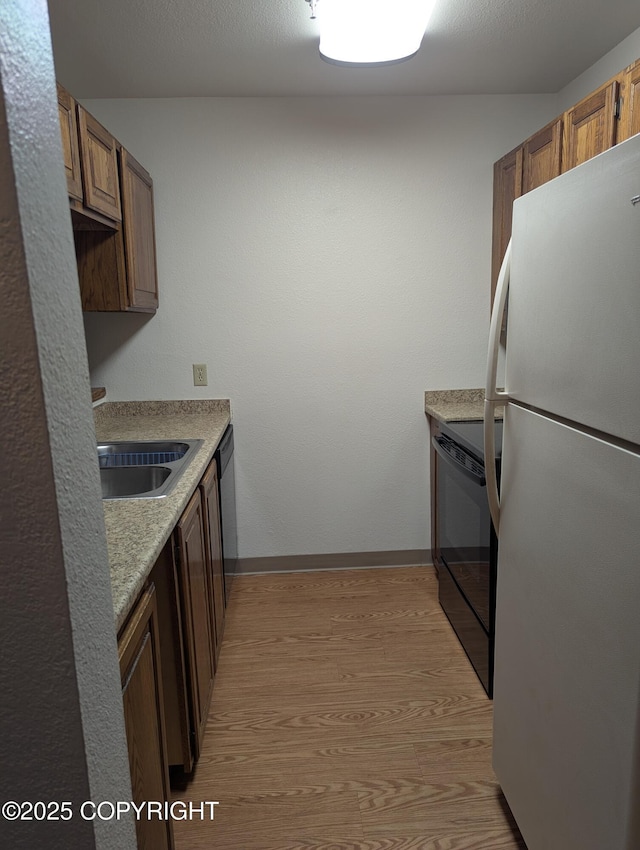 kitchen featuring light wood finished floors, black appliances, a sink, light countertops, and baseboards