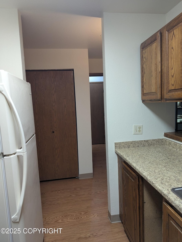 kitchen featuring light wood finished floors, light countertops, freestanding refrigerator, and baseboards